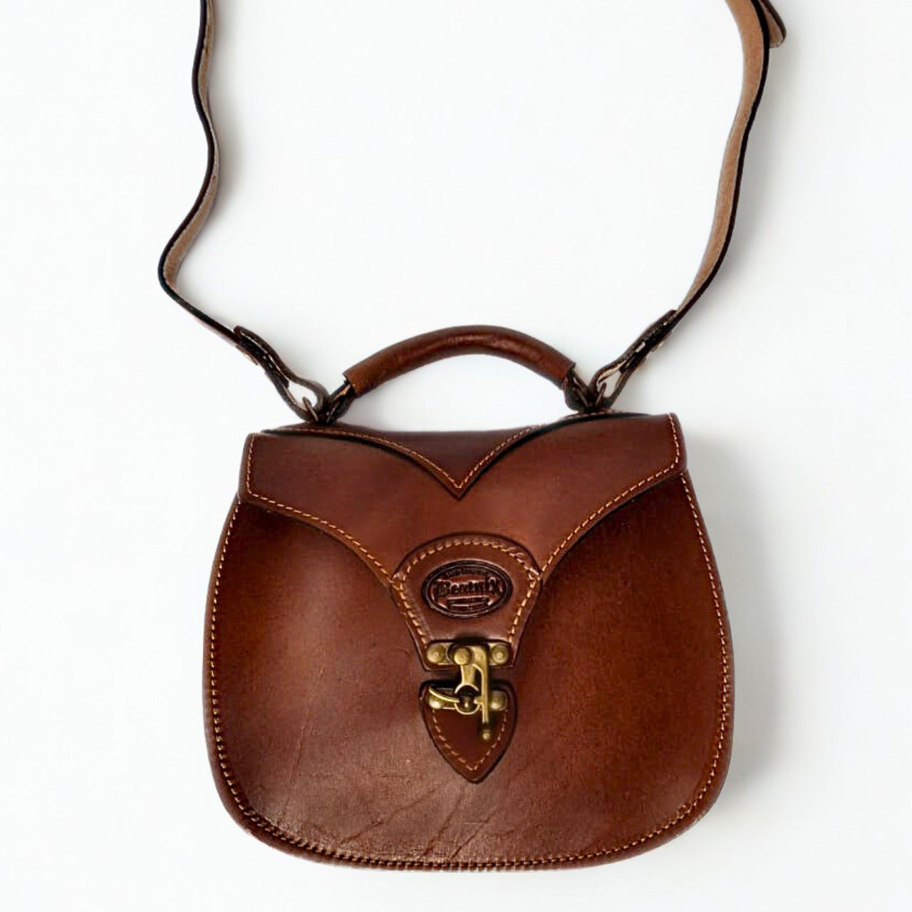 Beatnix Tinkie Brown Leather Sling Handbag – Crafted from genuine leather with contrast stitching and antique brass hardware. Features a structured design with a secure front clasp, top handle, and adjustable shoulder strap. Compact yet spacious with dimensions: 25cm (broad) x 22cm (high) x 10cm (deep). Perfect for everyday wear and classic styling. 3