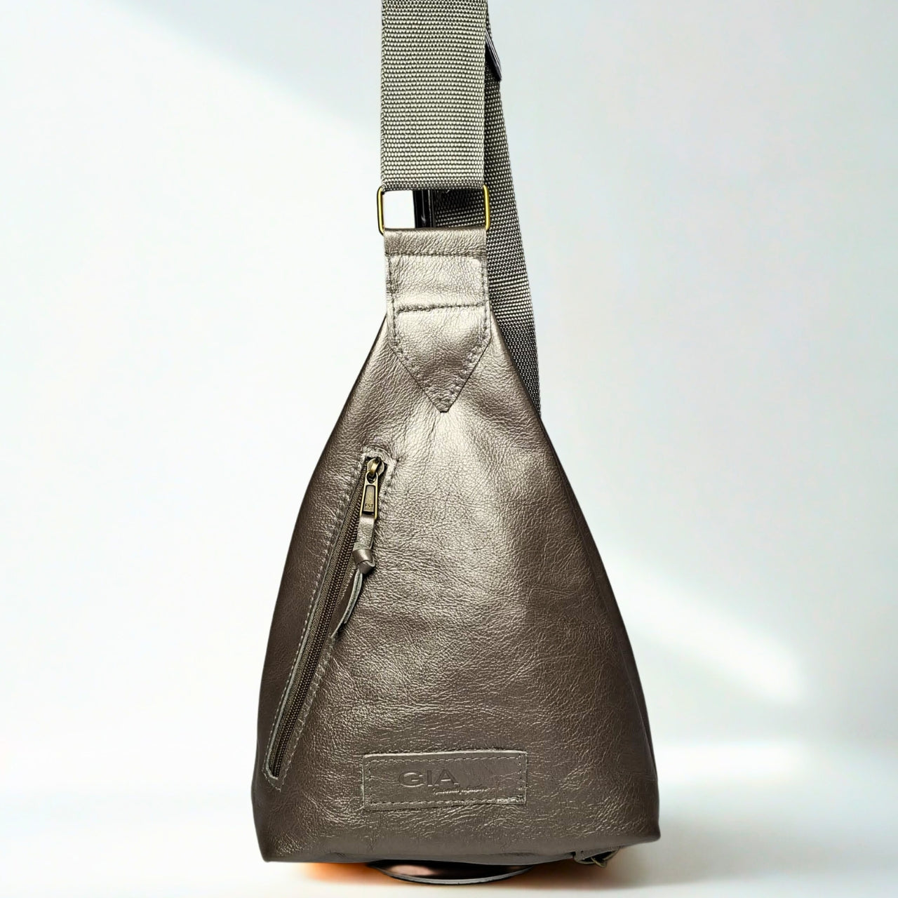 Gia Triangle Backpack in metallic pewter leather – modern triangular silhouette with gold-tone buckle, front and rear zip pockets, and embossed leather logo patch 1