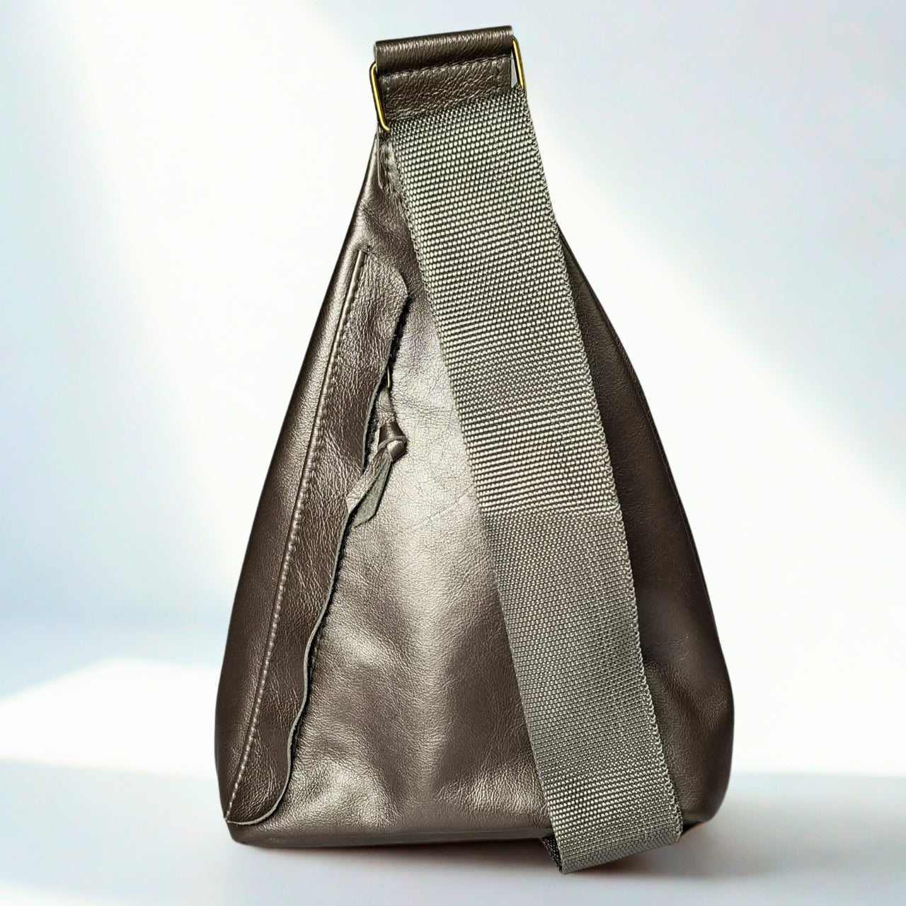 Gia Triangle Backpack in metallic pewter leather – modern triangular silhouette with gold-tone buckle, front and rear zip pockets, and embossed leather logo patch.
2