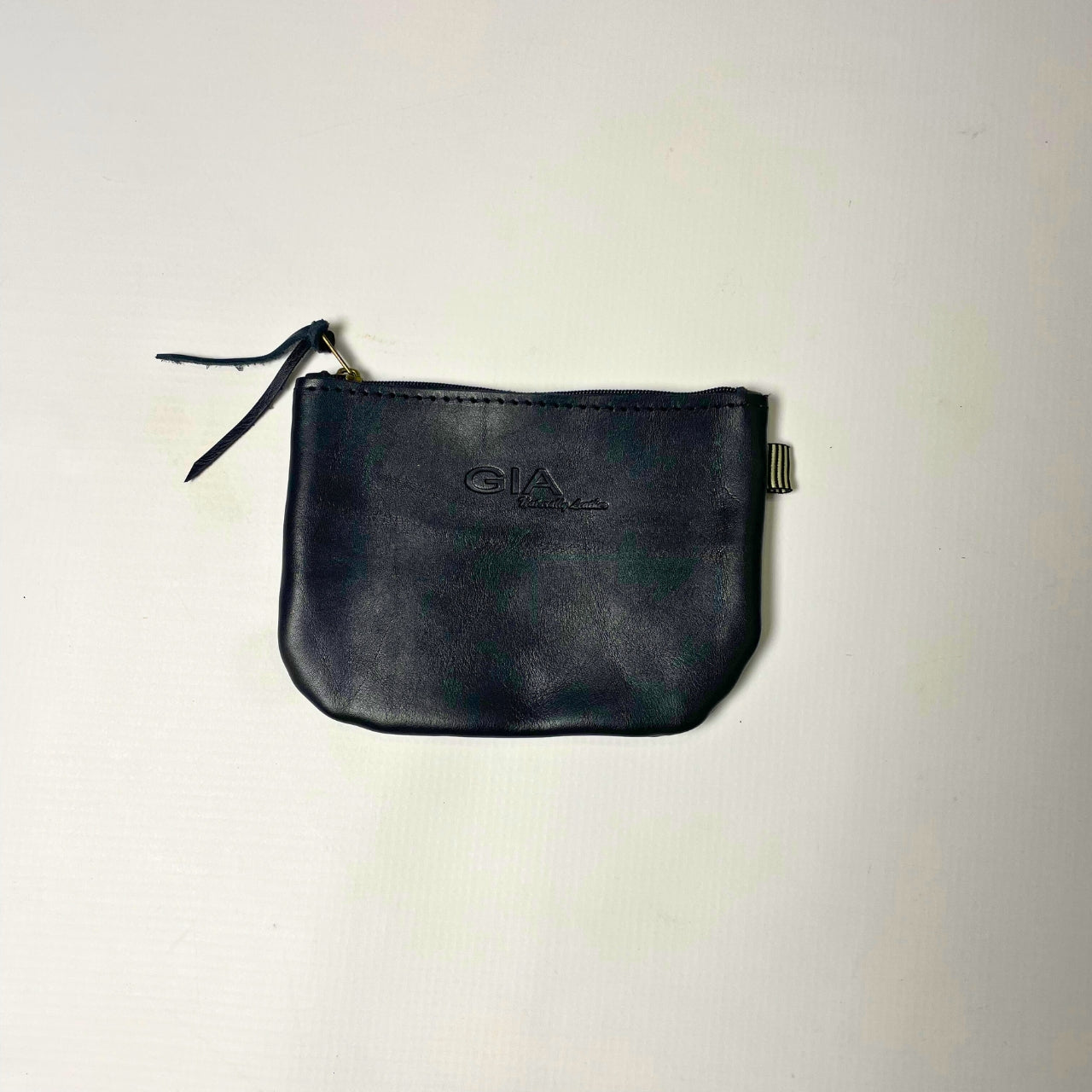 Gia Black Jenni Coin Purse, a compact genuine leather purse with a sleek, rounded design. Features an embossed GIA logo, zipper closure with a leather pull tab, and a stylish leather tassel. Ideal for coins, cards, and small essentials. Made in South Africa.