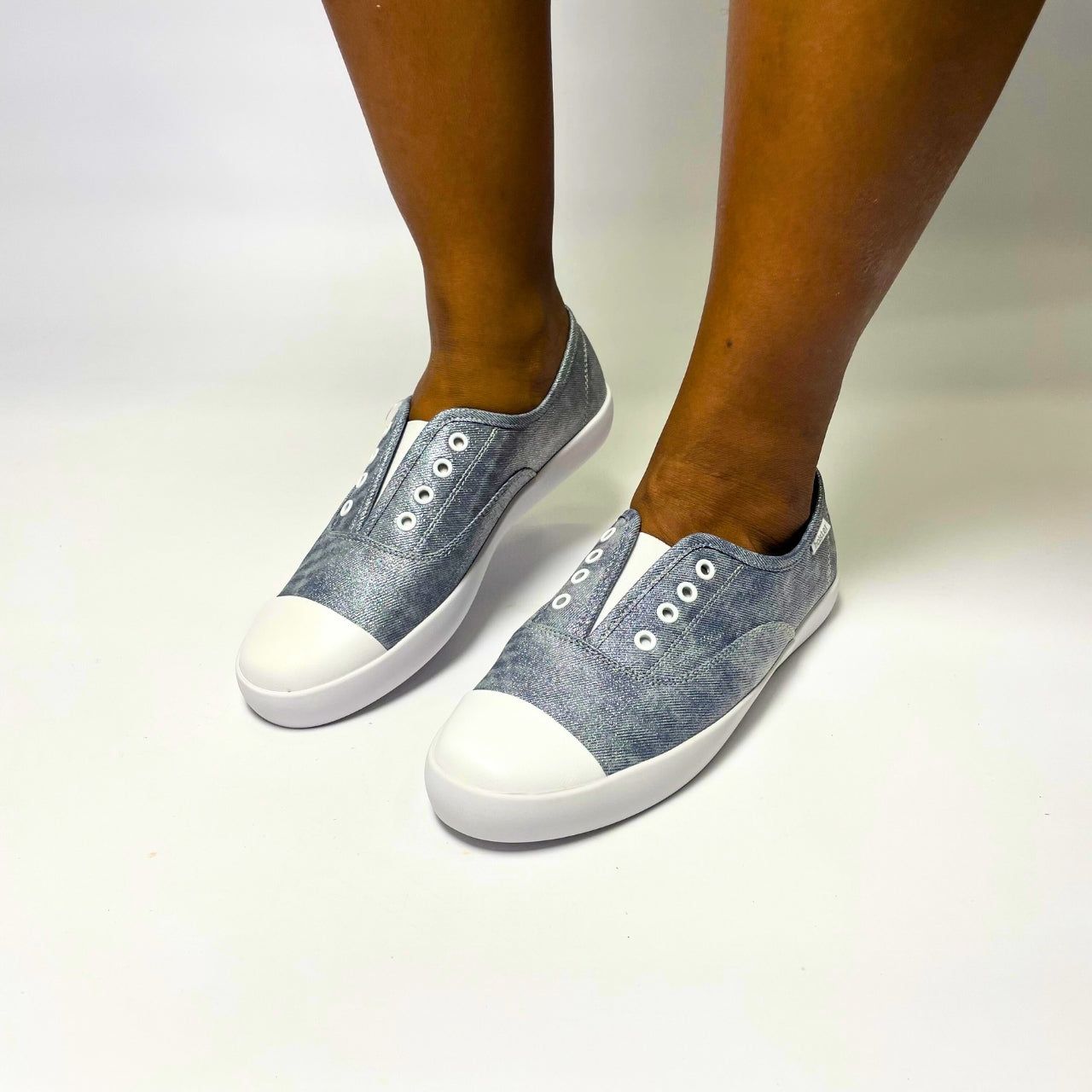 Holster Lulu Denim Shimmer Sneaker β Vegan-friendly, cruelty-free slip-on sneaker with a metallic PU upper and white PU toe cap. Features elastic gusset for easy wear, eyelet embellishments, and a soft PU foam insole for comfort. Designed with a non-slip rubber outsole and antibacterial properties. 1