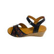 Gia black leather wedge sandals with laser-cut floral cross-over straps, cushioned insole, ankle strap, and natural wood finish heel – elegant women’s summer wedges for comfort and style.
