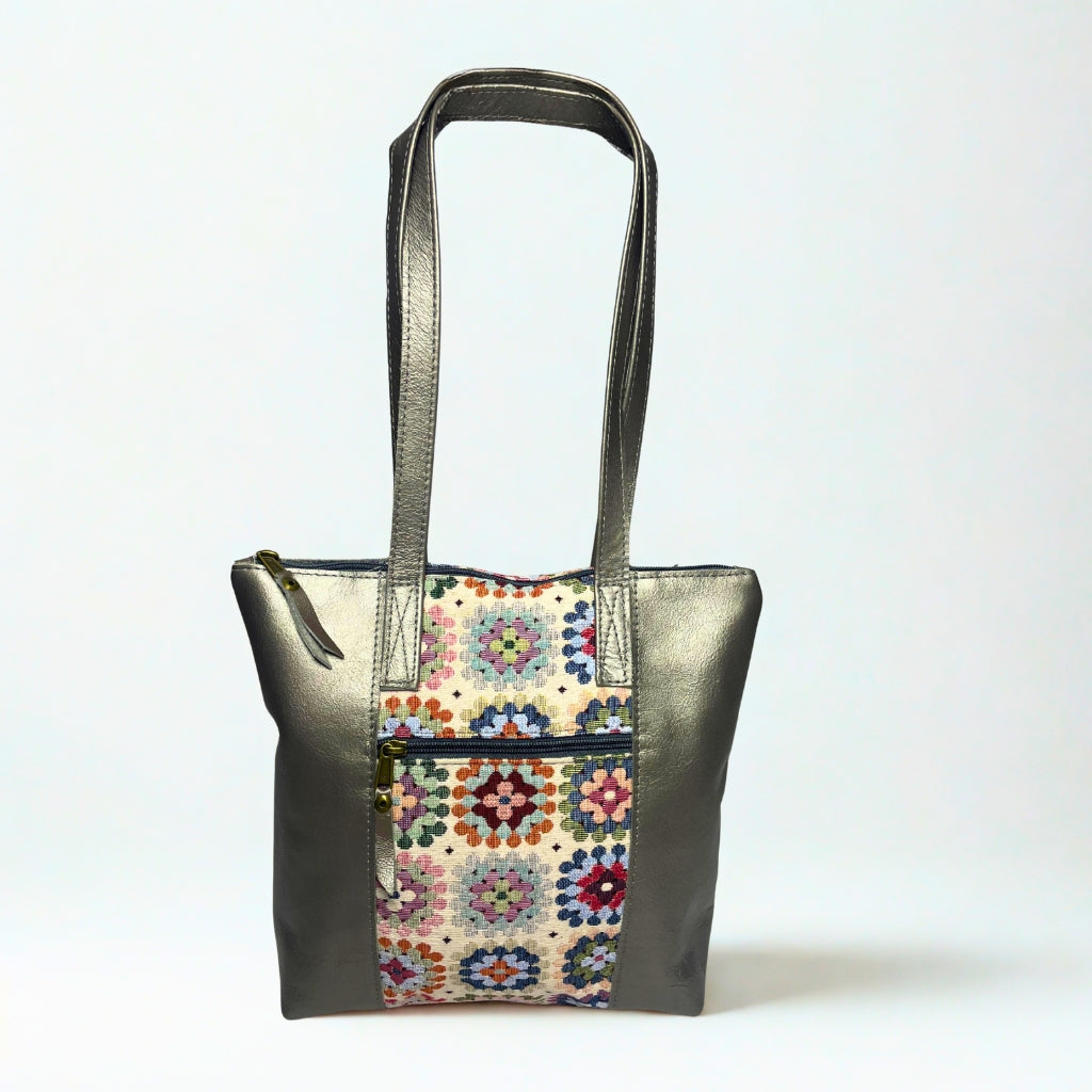 Gia pewter leather tote bag with woven tapestry panel, dual shoulder straps, antique brass hardware, and embossed logo – spacious crochet-inspired handbag for work, travel, and everyday style.